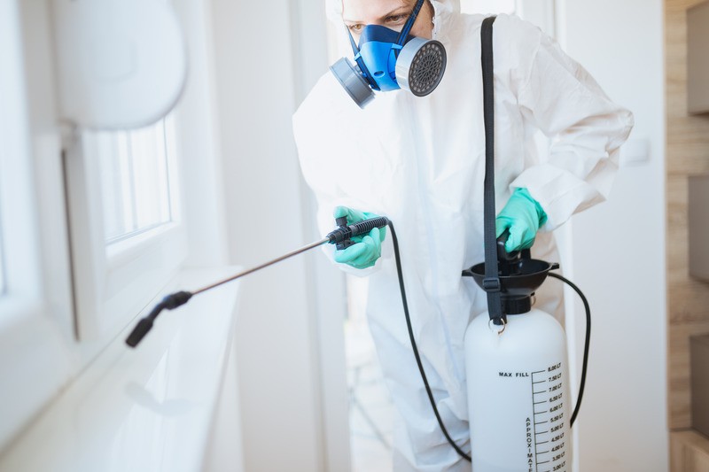 Persona in tuta protettiva spruzza disinfettante.