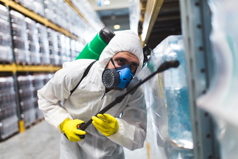 Persona in tuta protettiva spruzza disinfettante in magazzino.