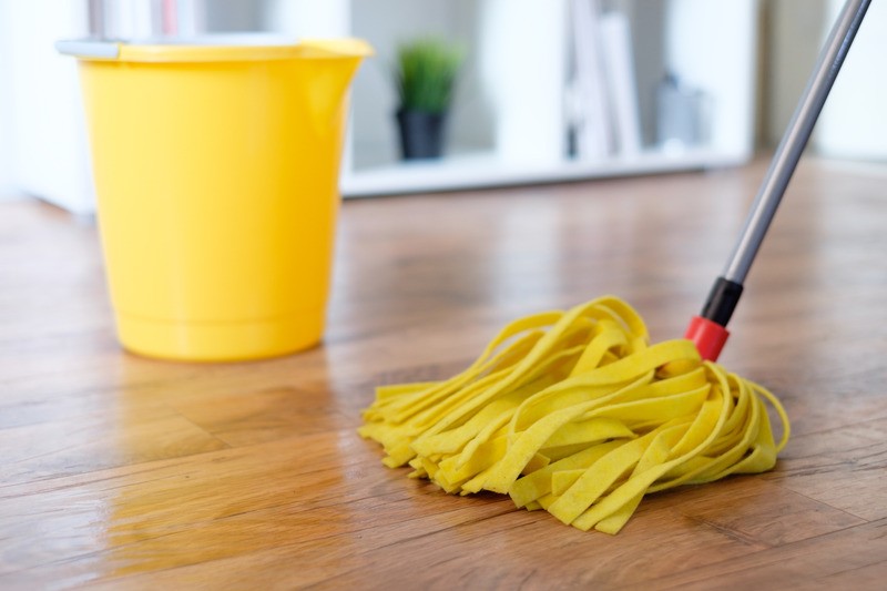 Mocio giallo e secchio su pavimento in legno.