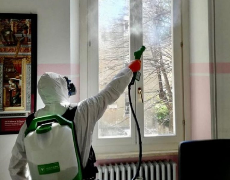 Persona in tuta protettiva disinfetta una finestra.